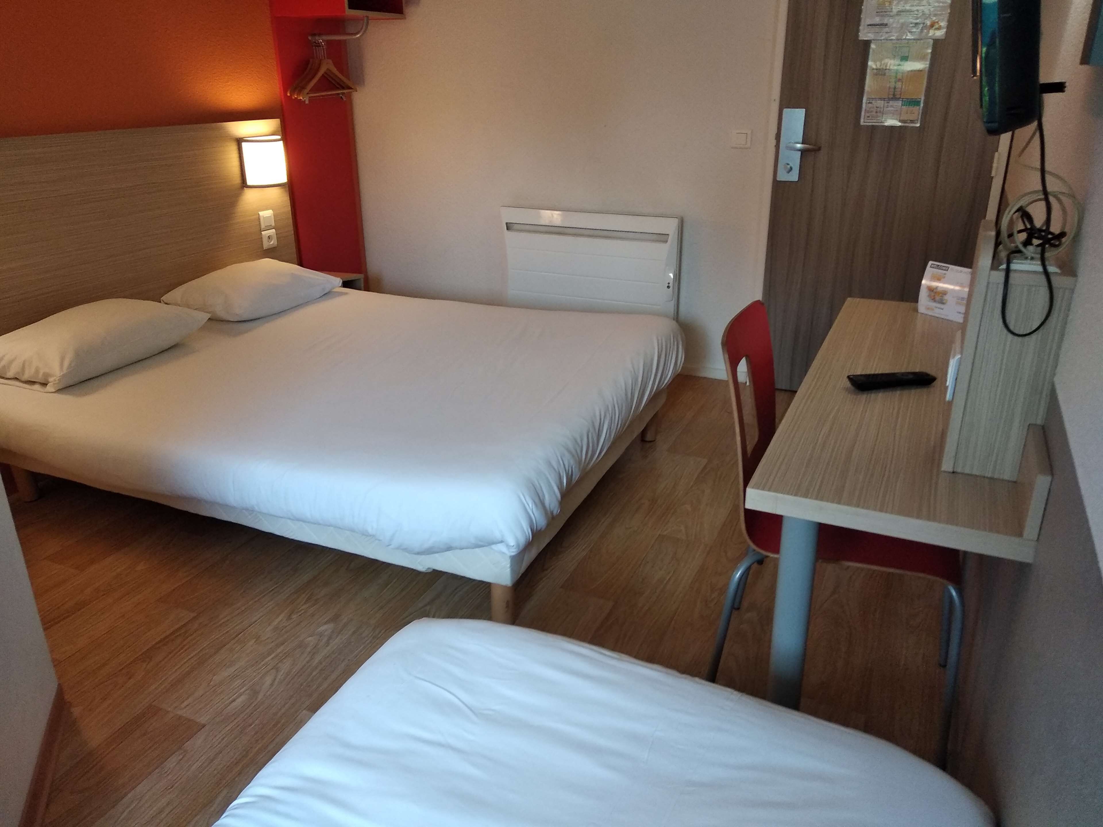 Quarto de hotel com duas camas, uma escrivaninha e uma cadeira.