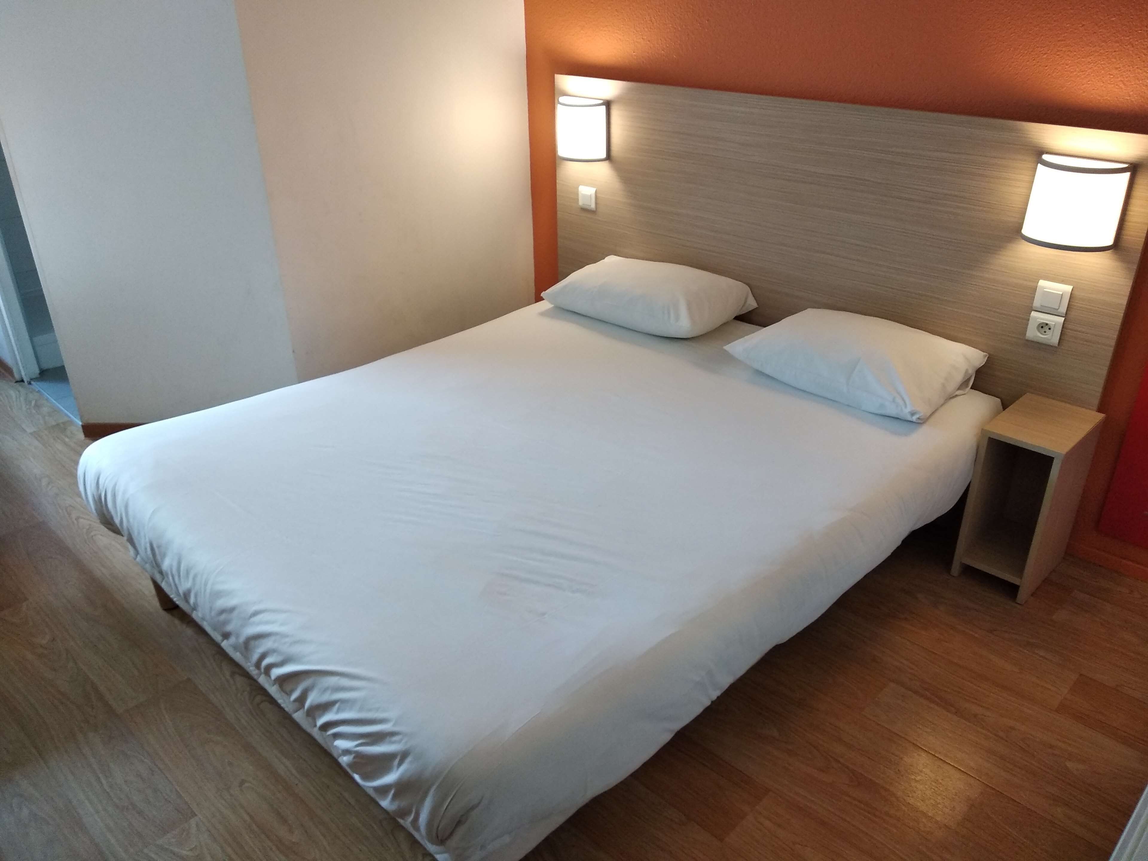 A neatly made bed with white linens, a wooden headboard, and two wall-mounted nightstands.