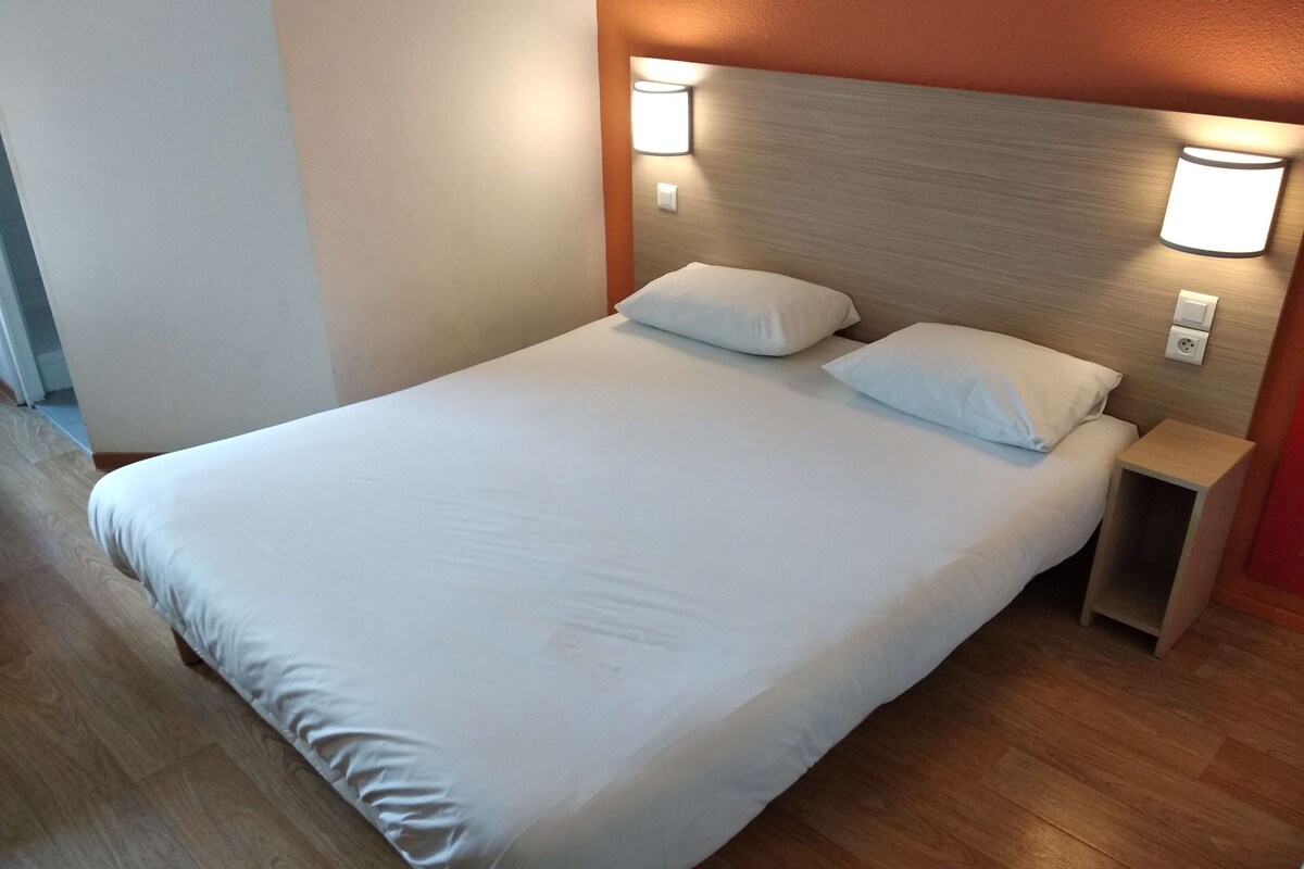 A neatly made bed with white linens, a wooden headboard, and two wall-mounted nightstands.