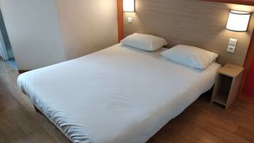 A neatly made bed with white linens, a wooden headboard, and two wall-mounted nightstands.