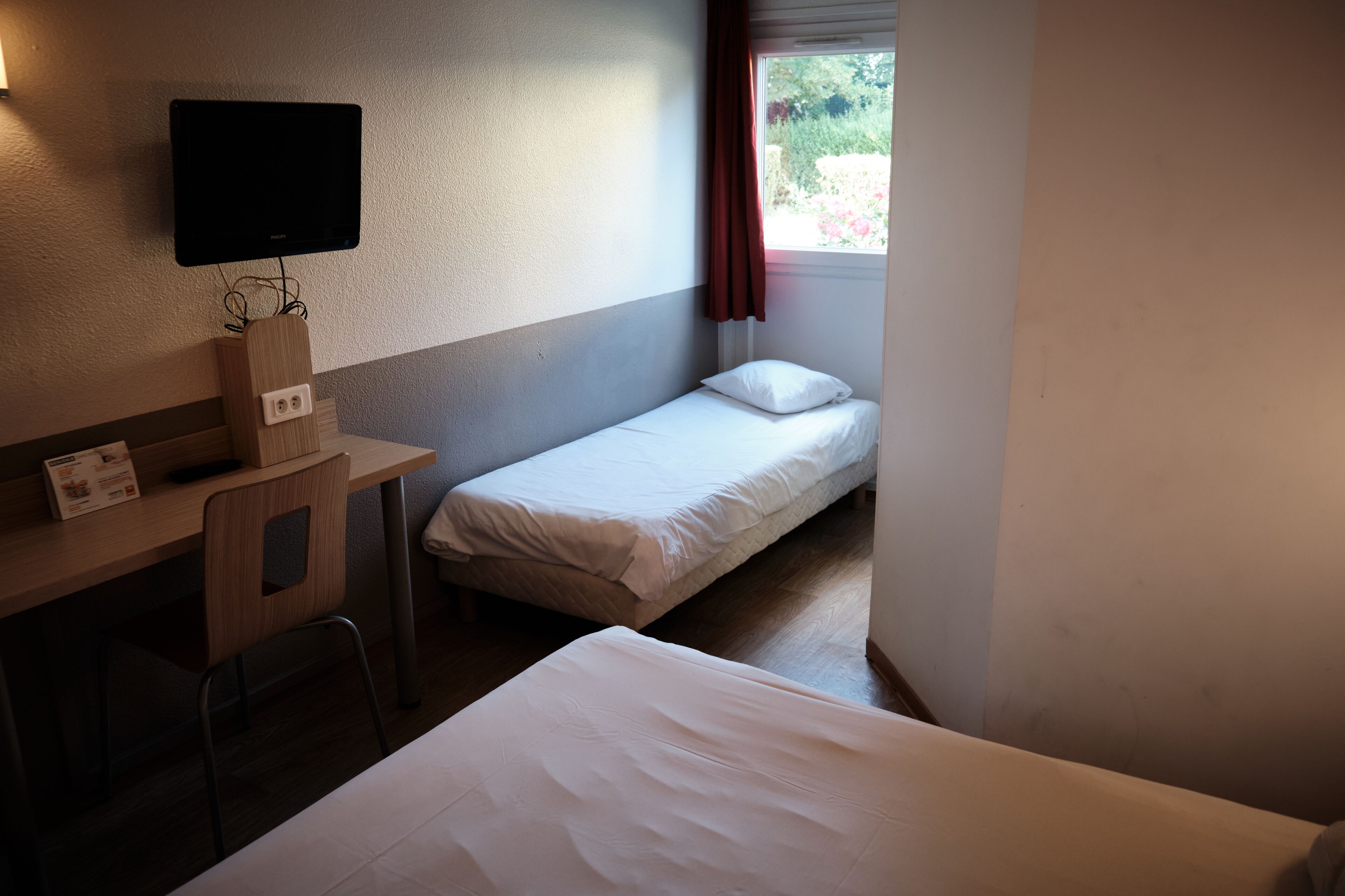 A small, clean room with a bed, a desk, and a TV.