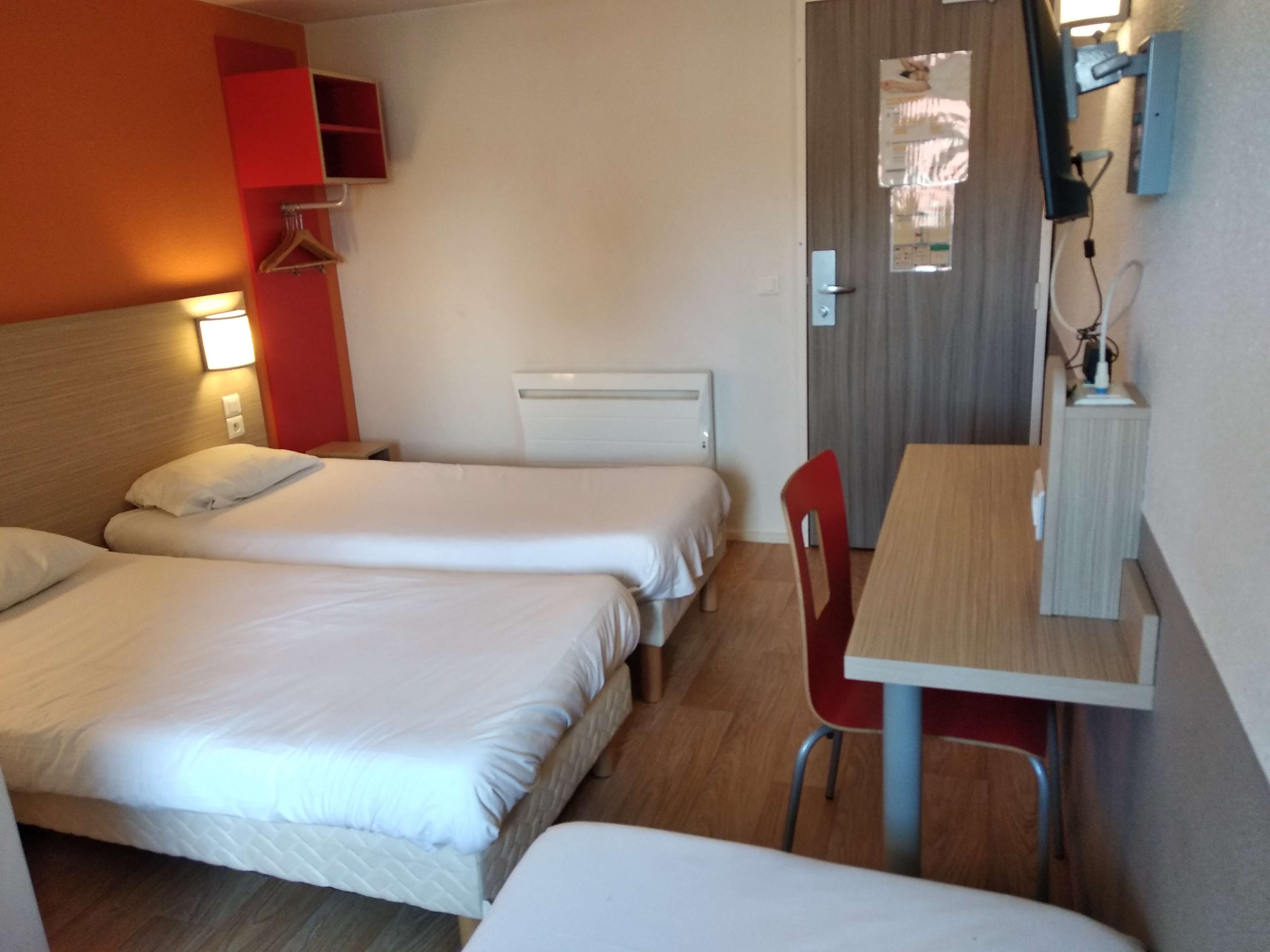 A hotel room with two beds, a desk, and a chair.