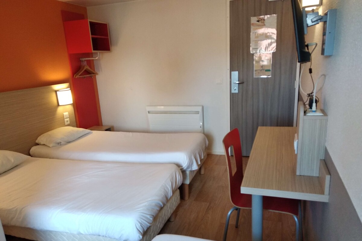 A hotel room with two beds, a desk, and a chair.