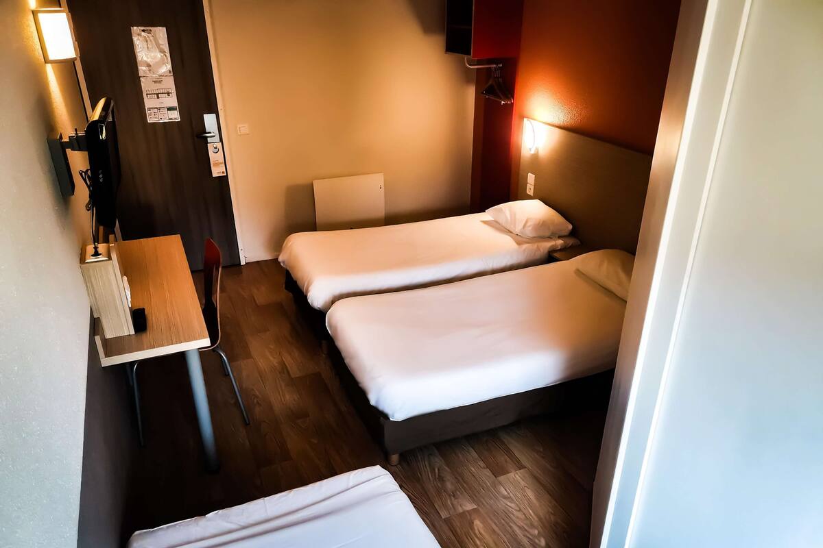 Ein kleines Hotelzimmer mit zwei Einzelbetten, einem Schreibtisch mit Stuhl und Holzboden.