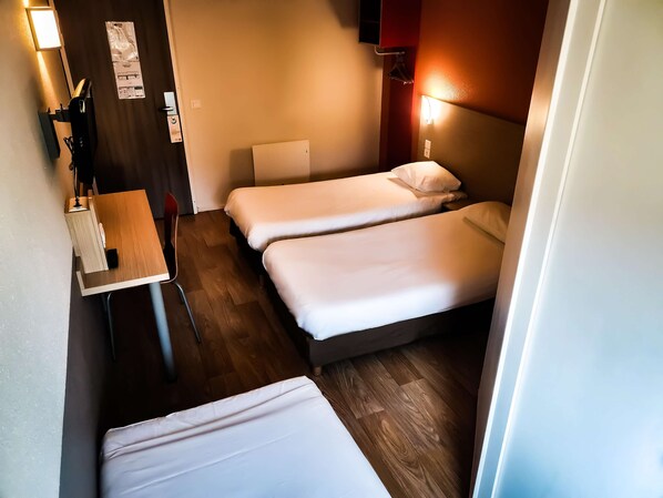 A compact hotel room with two single beds, a small desk with a chair, and a wooden floor.