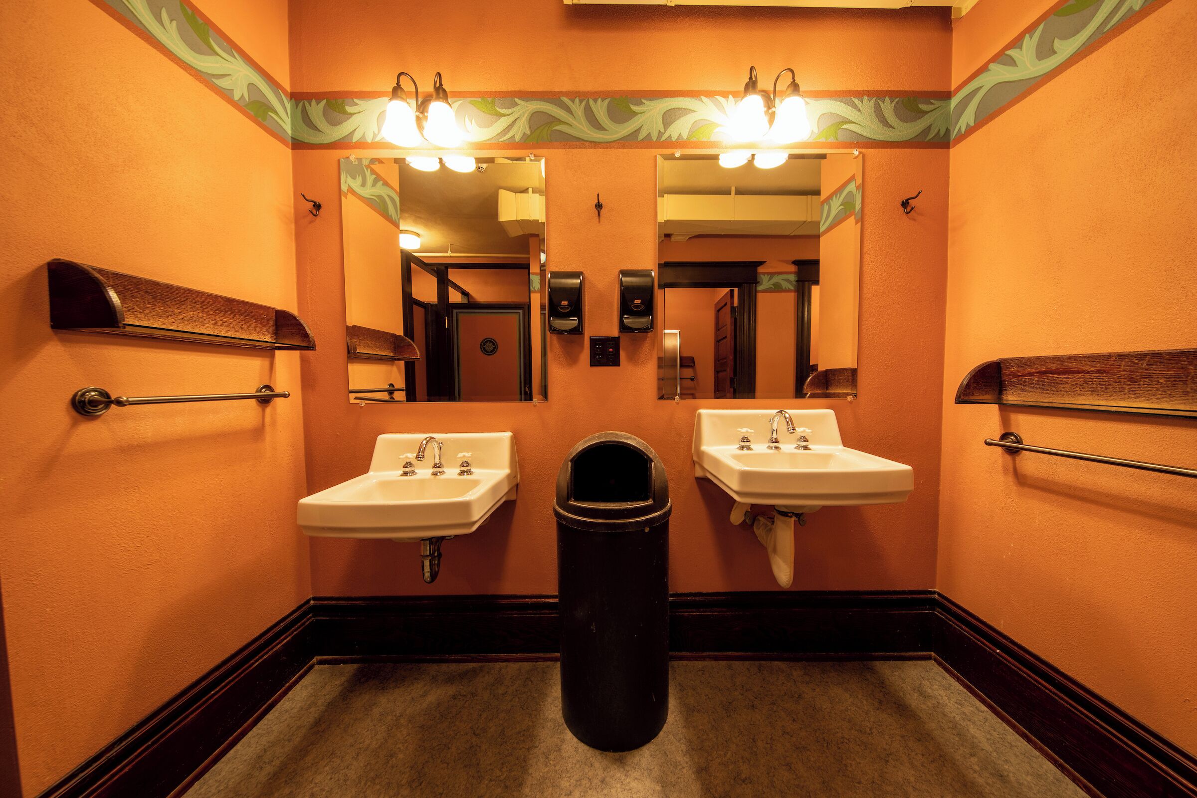 A bathroom with two sinks, a trash can, and a mirror.