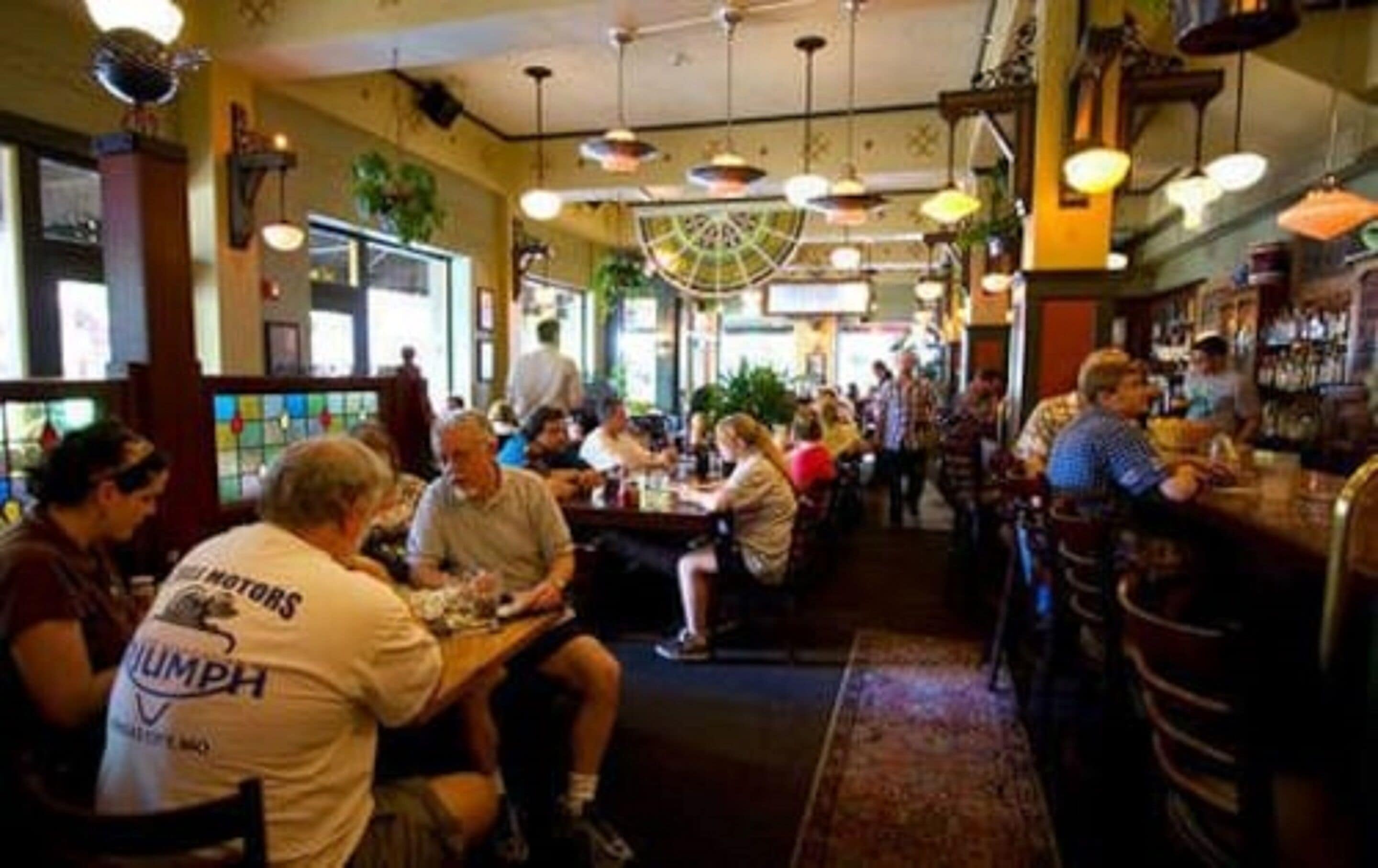 Ein belebtes Restaurant mit Gästen an Tischen, einer Bar mit Barkeeper und einer dekorativen Decke.