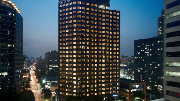 A high-rise building with illuminated windows at night, surrounded by other buildings and a busy street. - Shilla Stay Mapo Hongdae (Seoul)