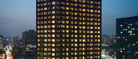 Un rascacielos con ventanas iluminadas, presumiblemente un hotel, rodeado por un paisaje urbano al atardecer.