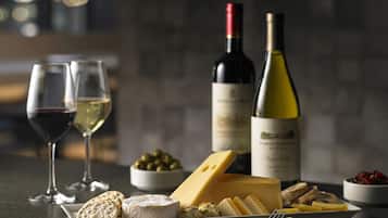 A cheese platter with various cheeses, crackers, and olives, accompanied by two wine glasses and bottles of wine on a table.