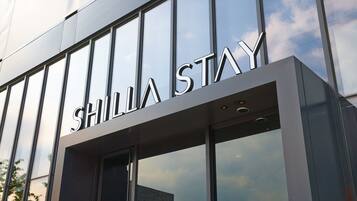 SHILIA STAY's sleek exterior showcases its modern design with large glass windows reflecting the surroundings.