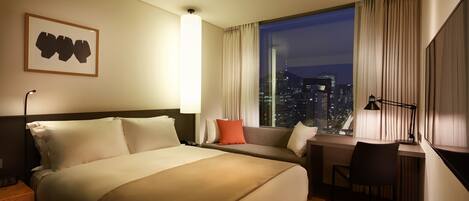 A hotel room with a large bed, a desk, and a view of the city at night.