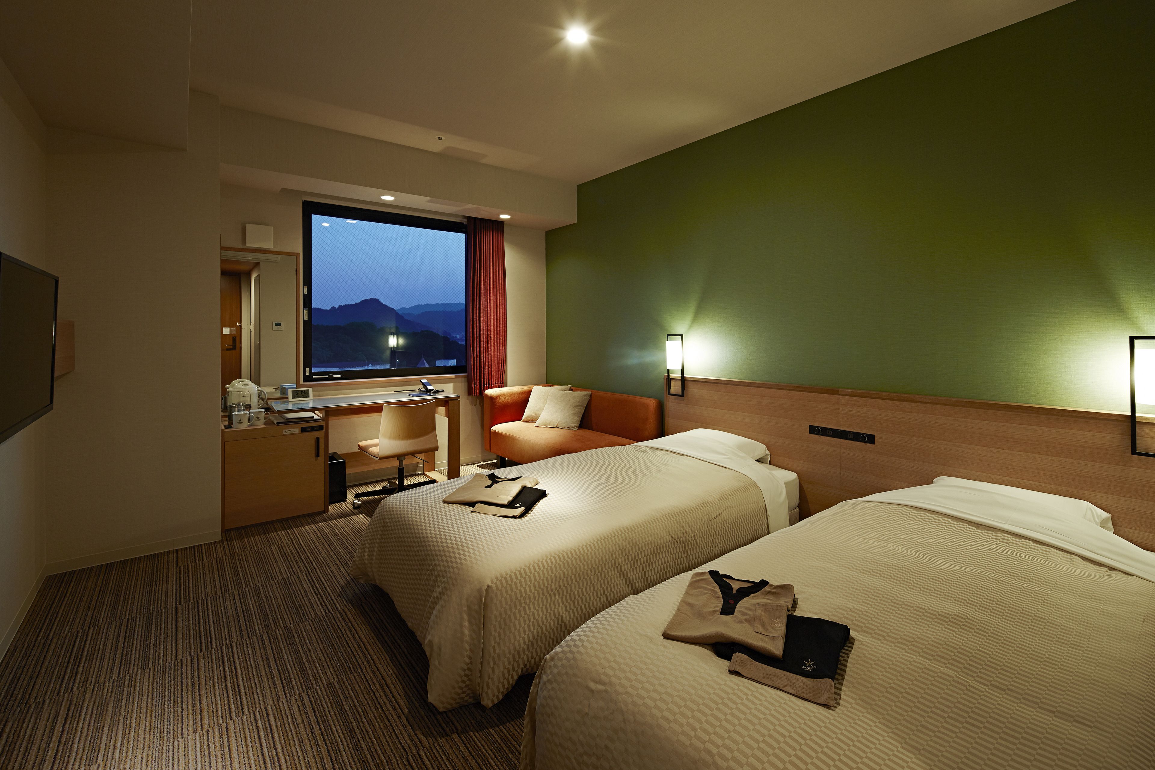 Ein Hotelzimmer mit zwei Betten, einem Schreibtisch, einem Sessel, einem Fernseher und Bergblick.