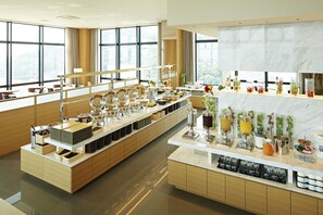 Espaço de café da manhã de um hotel moderno, com um balcão longo, sistema de buffet e grandes janelas com vista para a cidade.