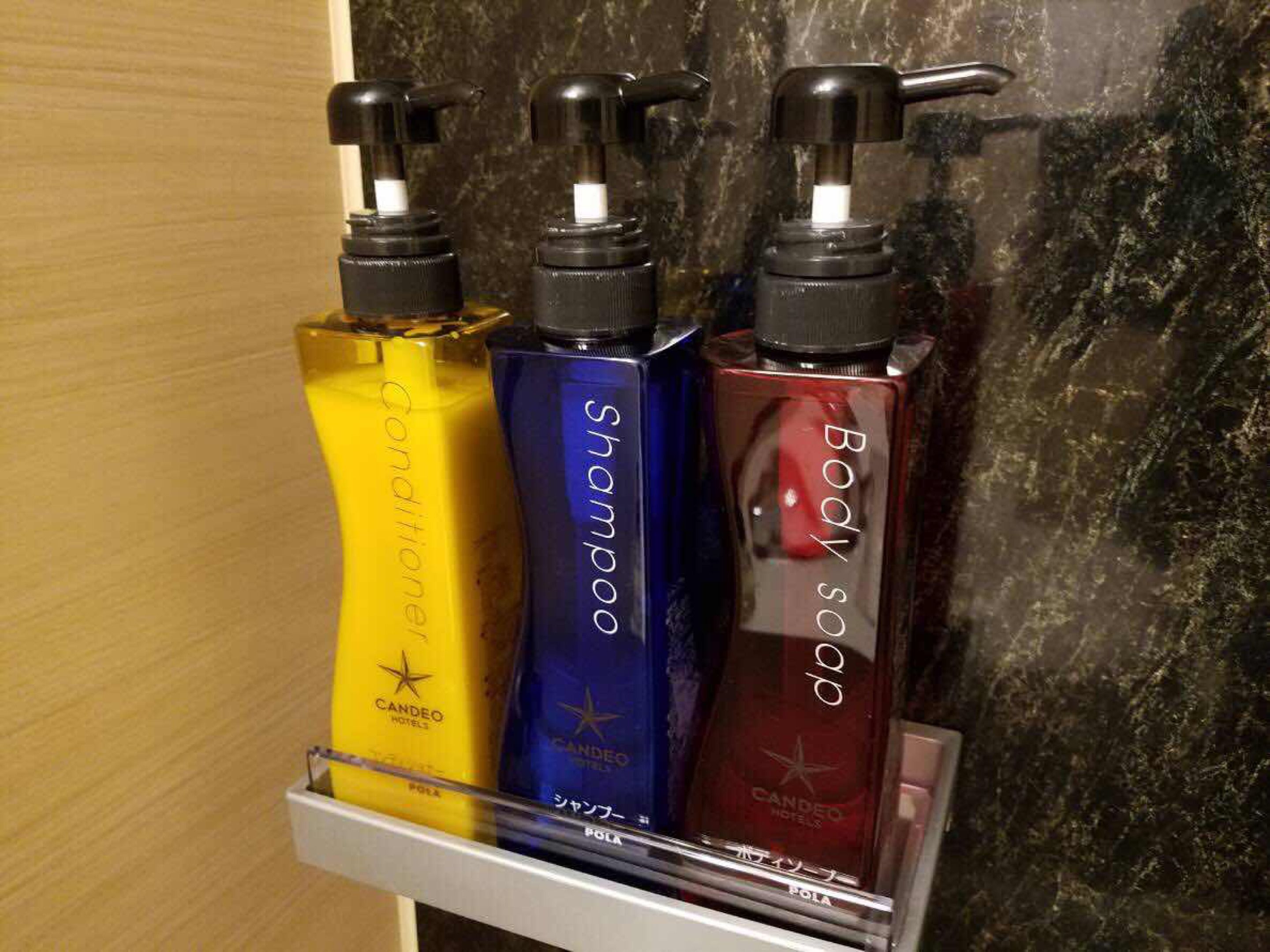 Un ensemble de trois produits de toilette présentés dans un distributeur mural dans la salle de bain d’un hôtel.
