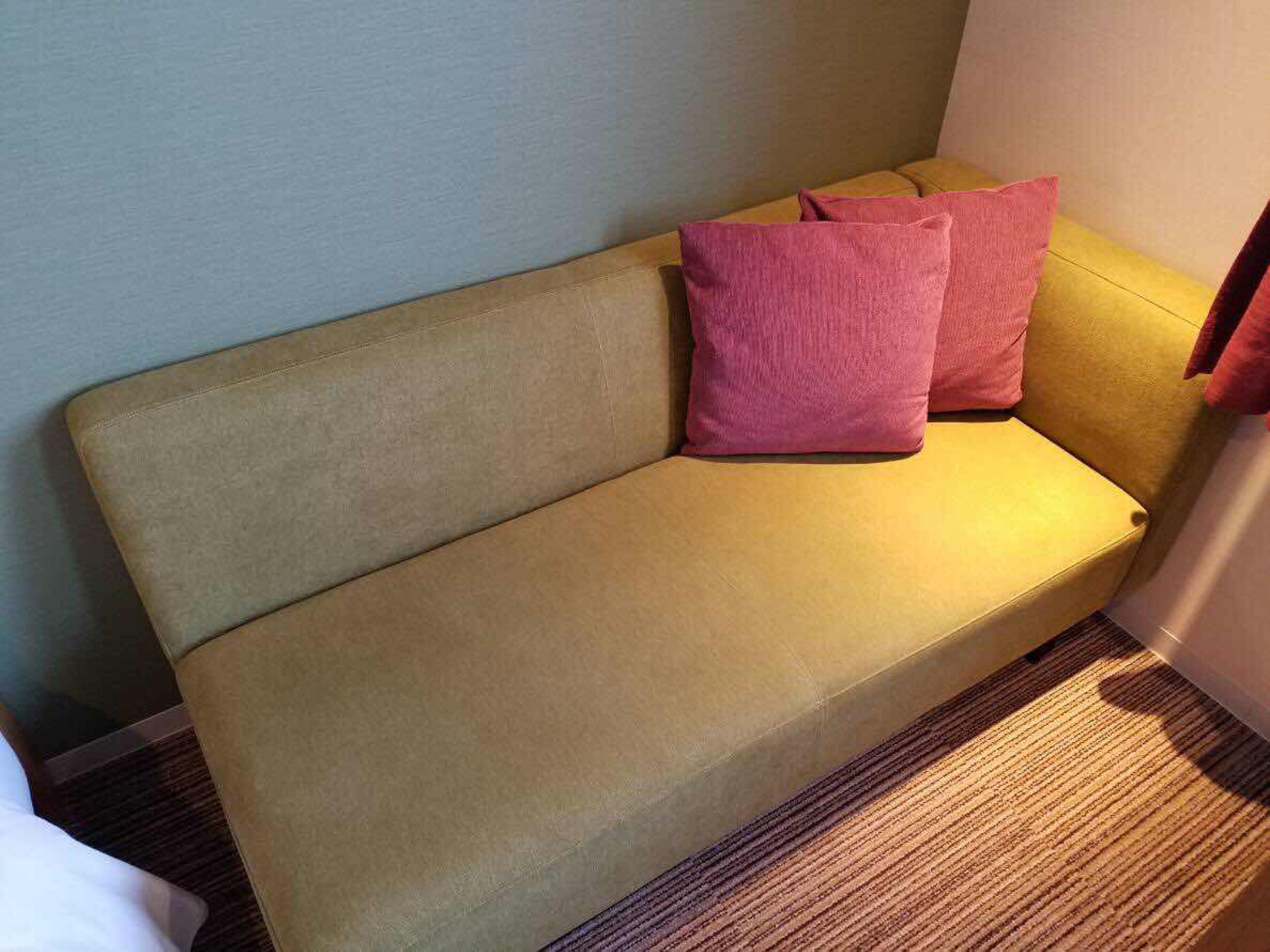 A beige sofa with two pink cushions in a room with a carpeted floor.