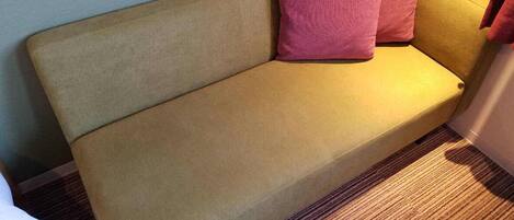 A beige sofa with two pink cushions in a room with a carpeted floor.
