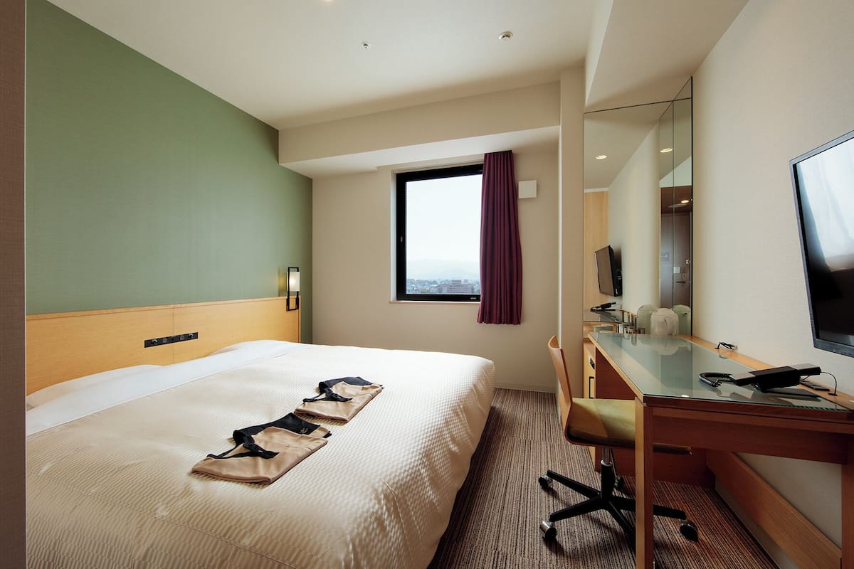 Ein Hotelzimmer mit Bett, Schreibtisch, Stuhl, Fernseher und einem Fenster mit Blick.