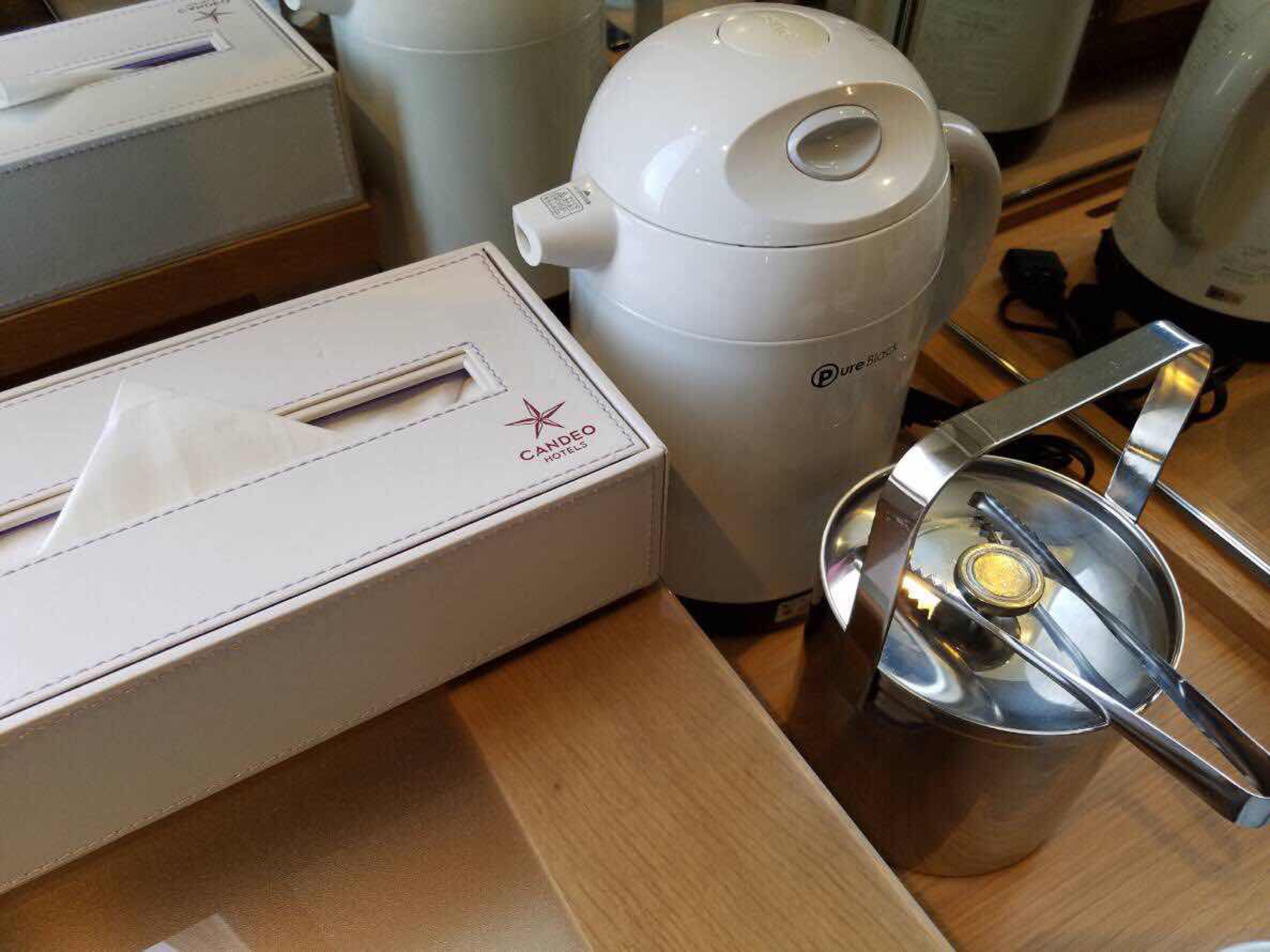 A coffee maker, a box labeled "Candeo Hotels," and a metal strainer on a wooden surface.