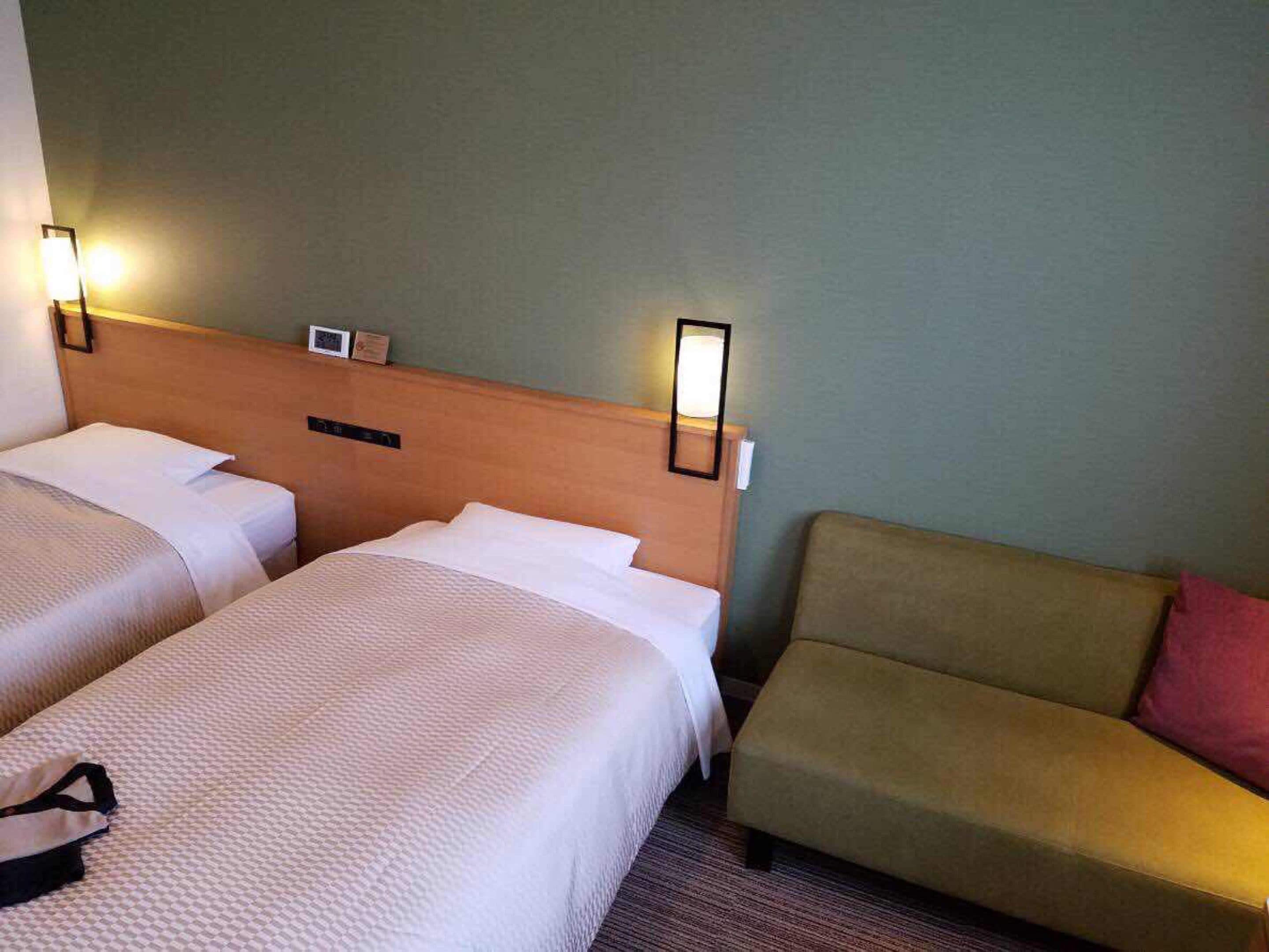 A hotel room with two beds, a nightstand, and a sofa.