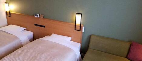 A hotel room with two beds, a nightstand, and a sofa.