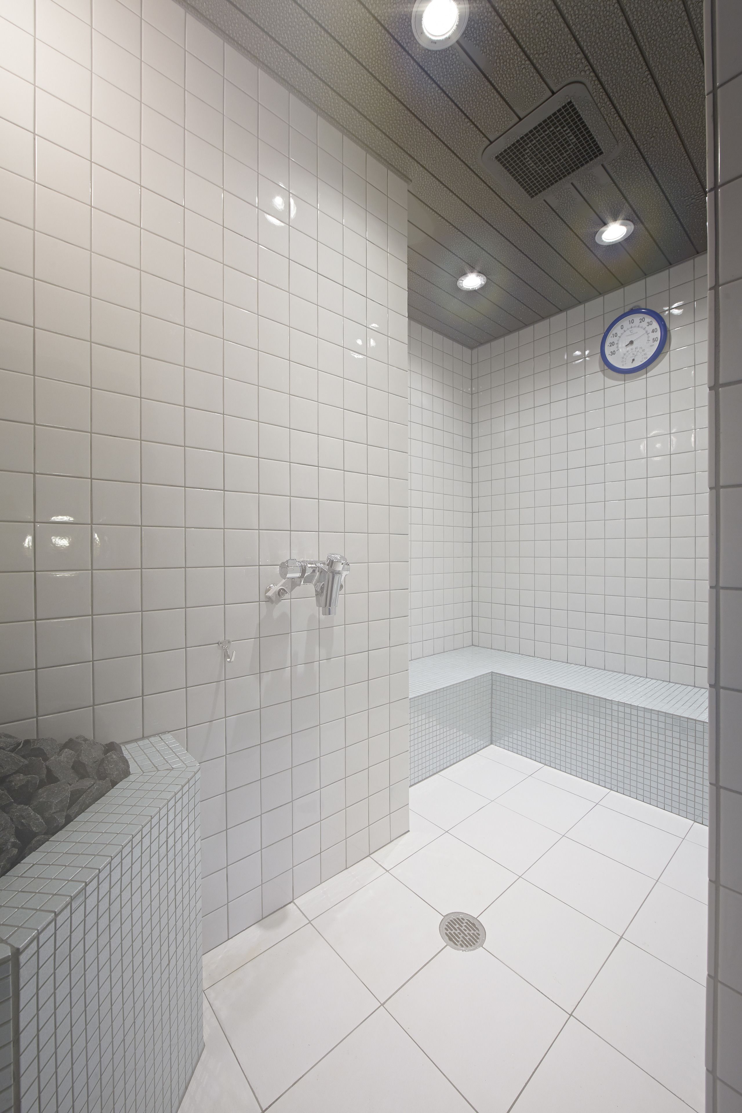 A modern bathroom with white tiles, a built-in shower, and a visible water heater.