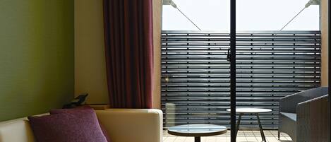 A hotel room with a bed, a sofa, a small table, and a balcony with a view.