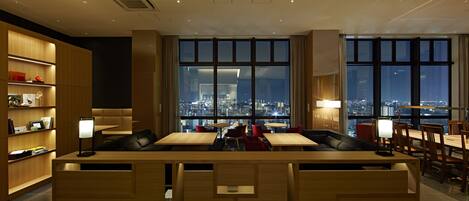 Un moderno vestíbulo de hotel con una recepción, zona de estar y grandes ventanales con vistas a la ciudad.