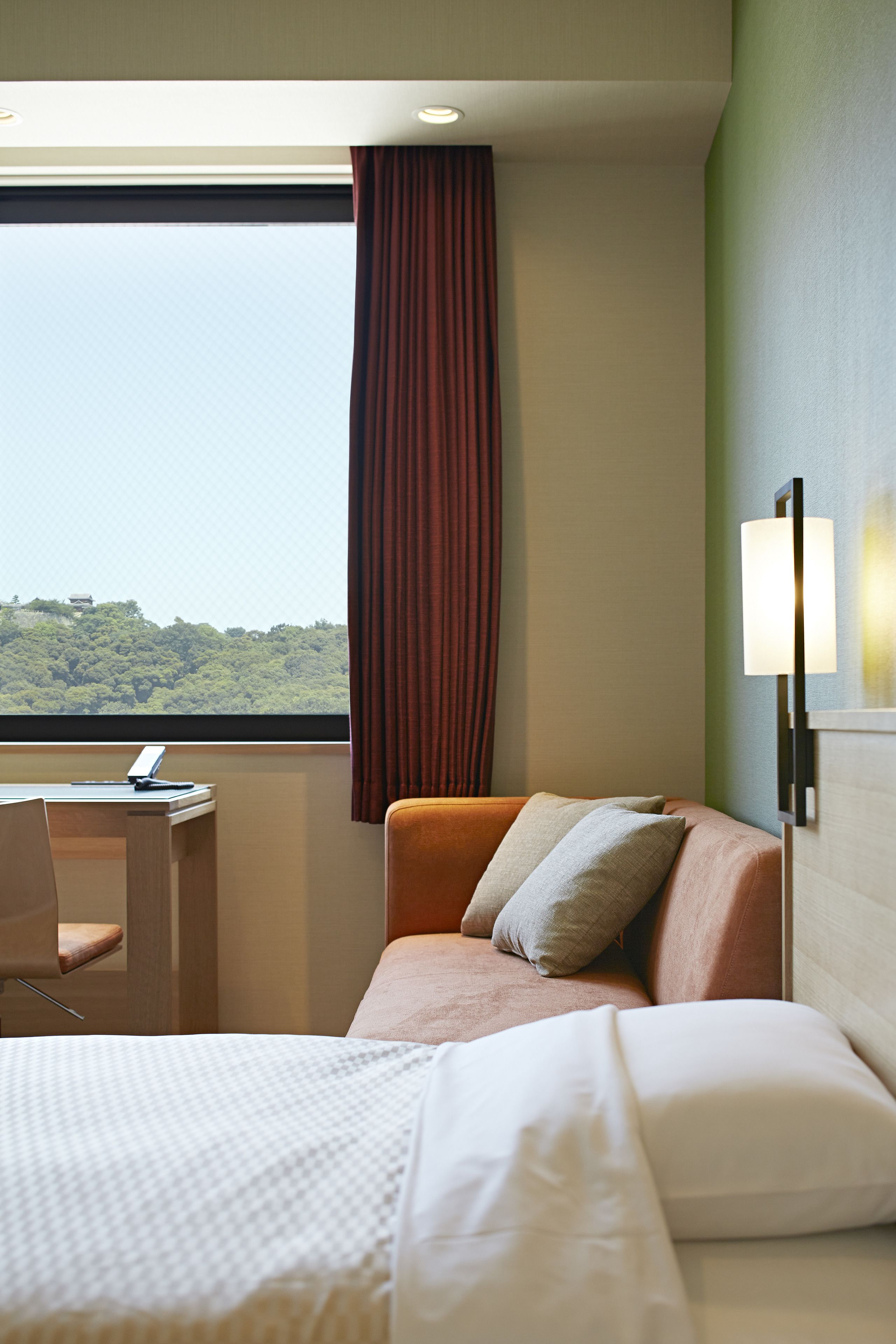 Een hotelkamer met een bed, een bureau en uitzicht op een bebost gebied.