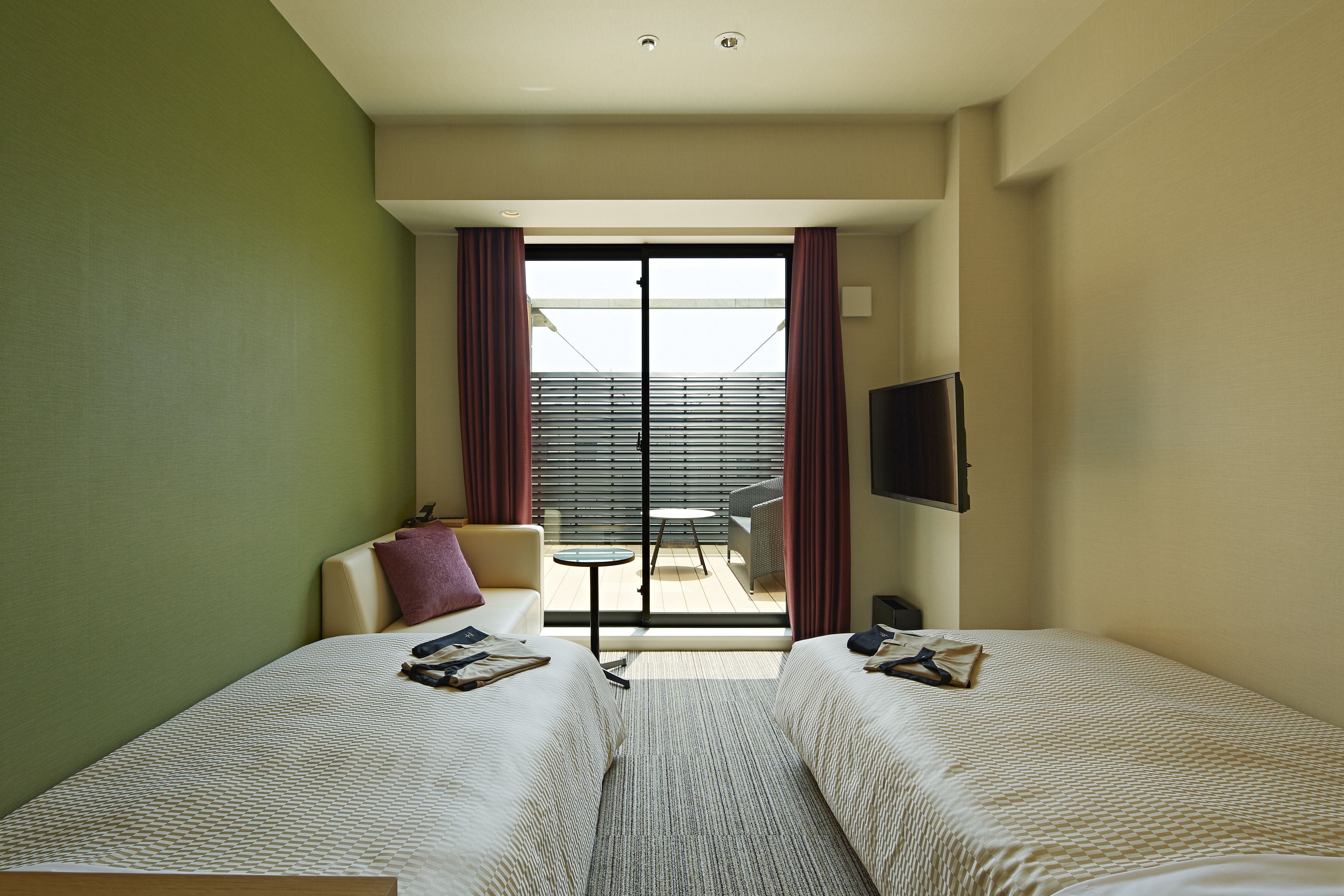 A hotel room with two beds, a sofa, a small table, and a TV.