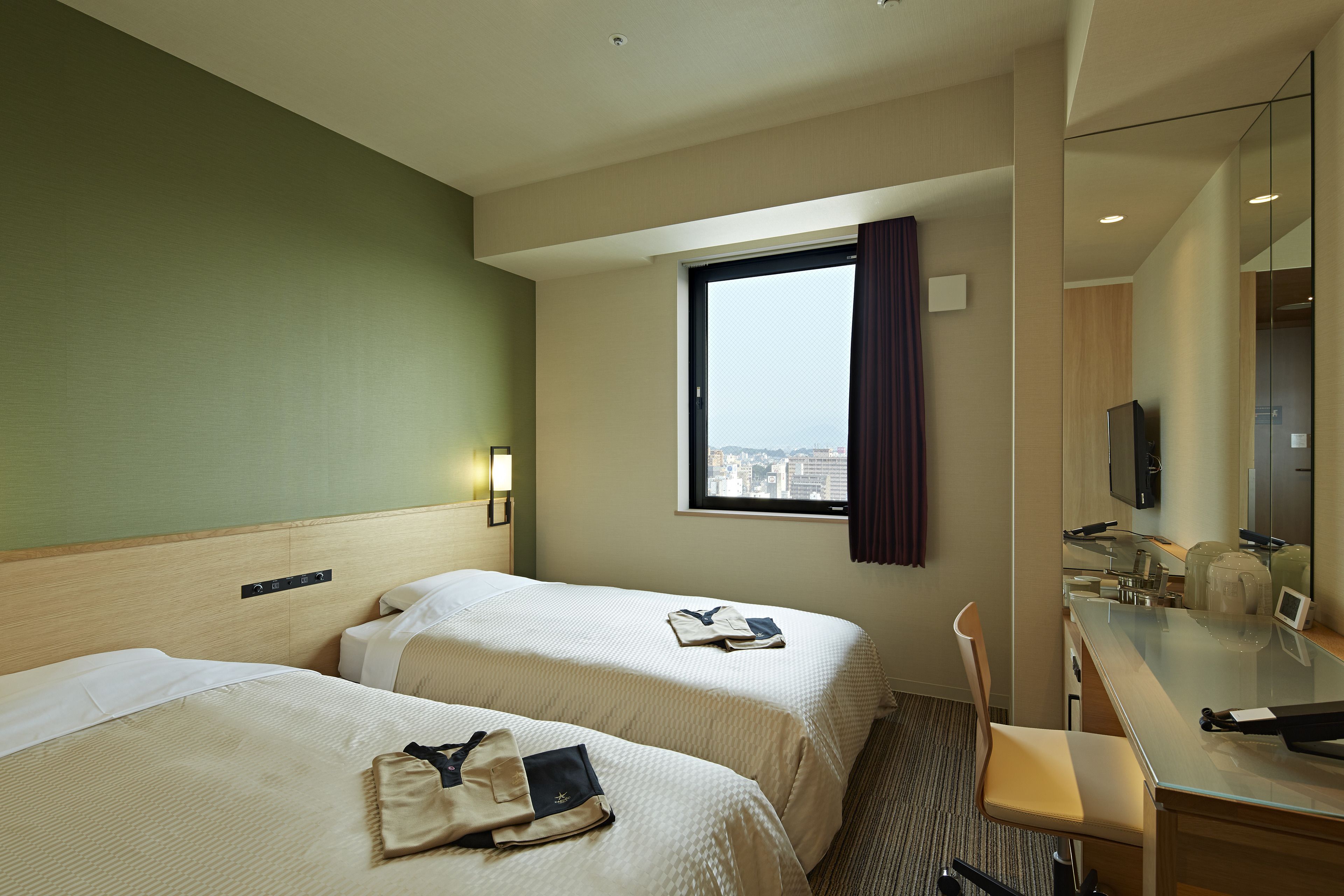 Een hotelkamer met twee bedden, een bureau, een stoel, een raam met gordijnen en een televisie.