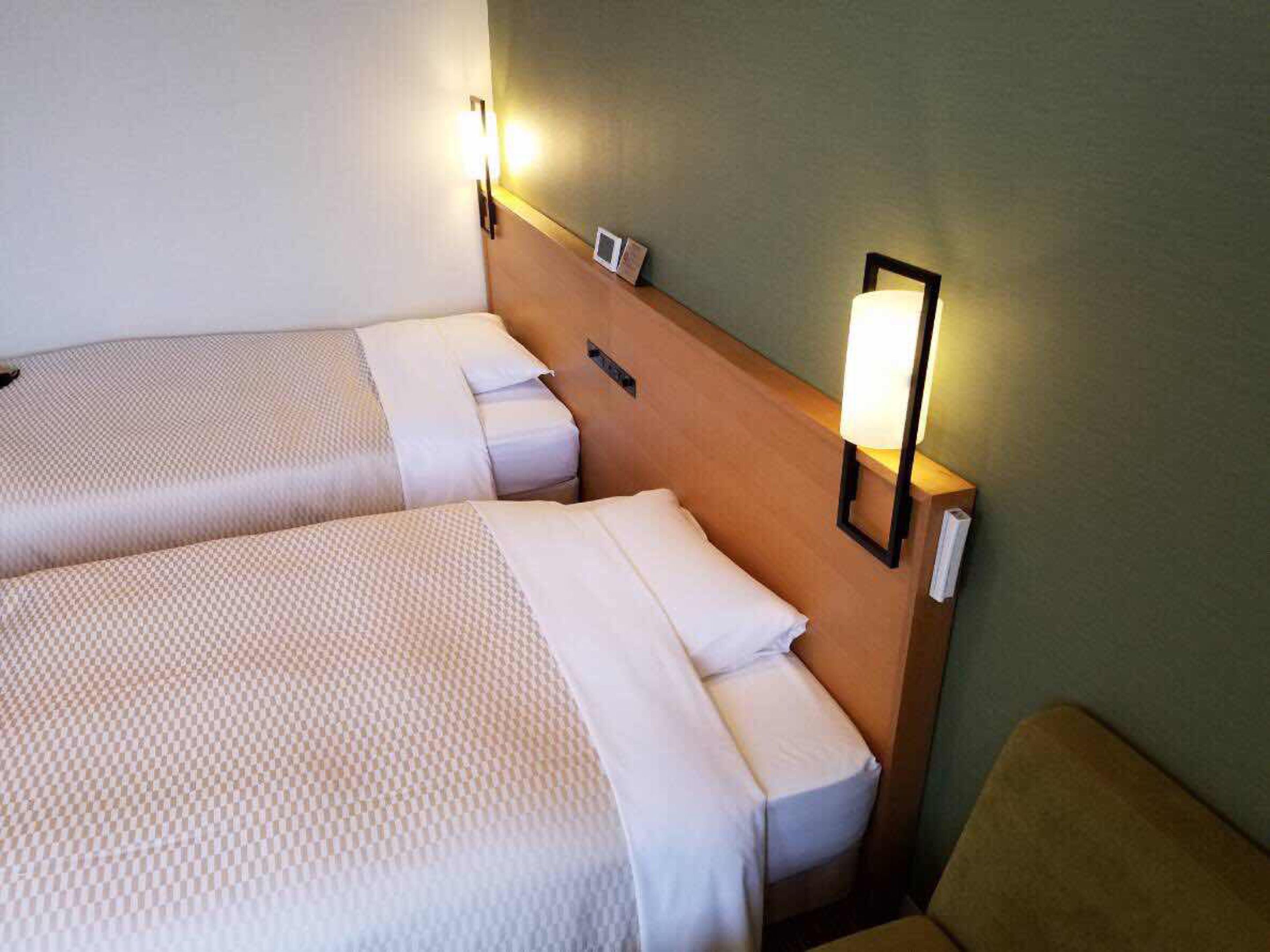 Hotellihuone, jossa on kaksi erillistä sänkyä, puinen pääty ja seinään kiinnitetyt valaisimet.