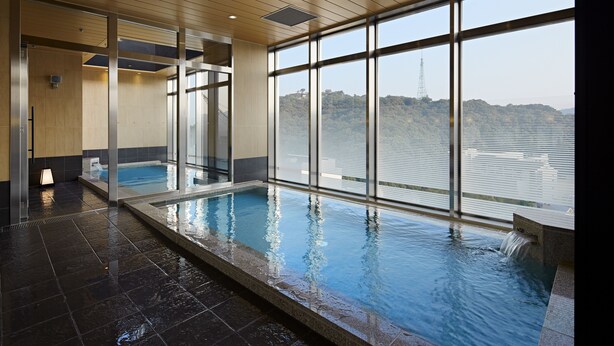 An indoor swimming pool with a view of a body of water and hills. - Candeo Hotels Matsuyama Okaido (Matsuyama)