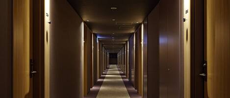 Corredor longo e estreito de um hotel, com portas de madeira em ambos os lados e piso coberto de carpete.
