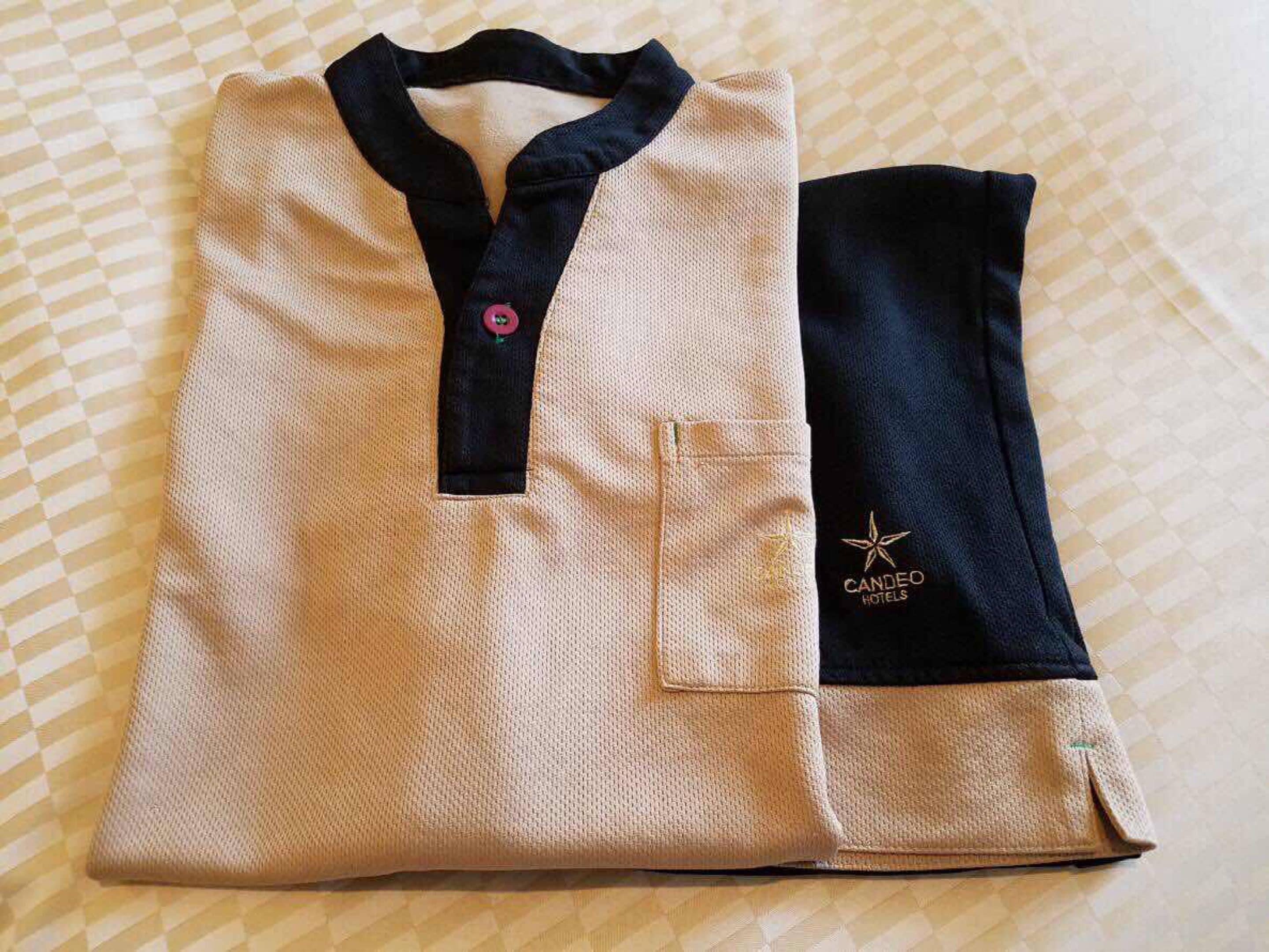 Un uniforme d’hôtel, de couleur beige et bleu marine, soigneusement plié, orné d’un logo et doté d’une poche.