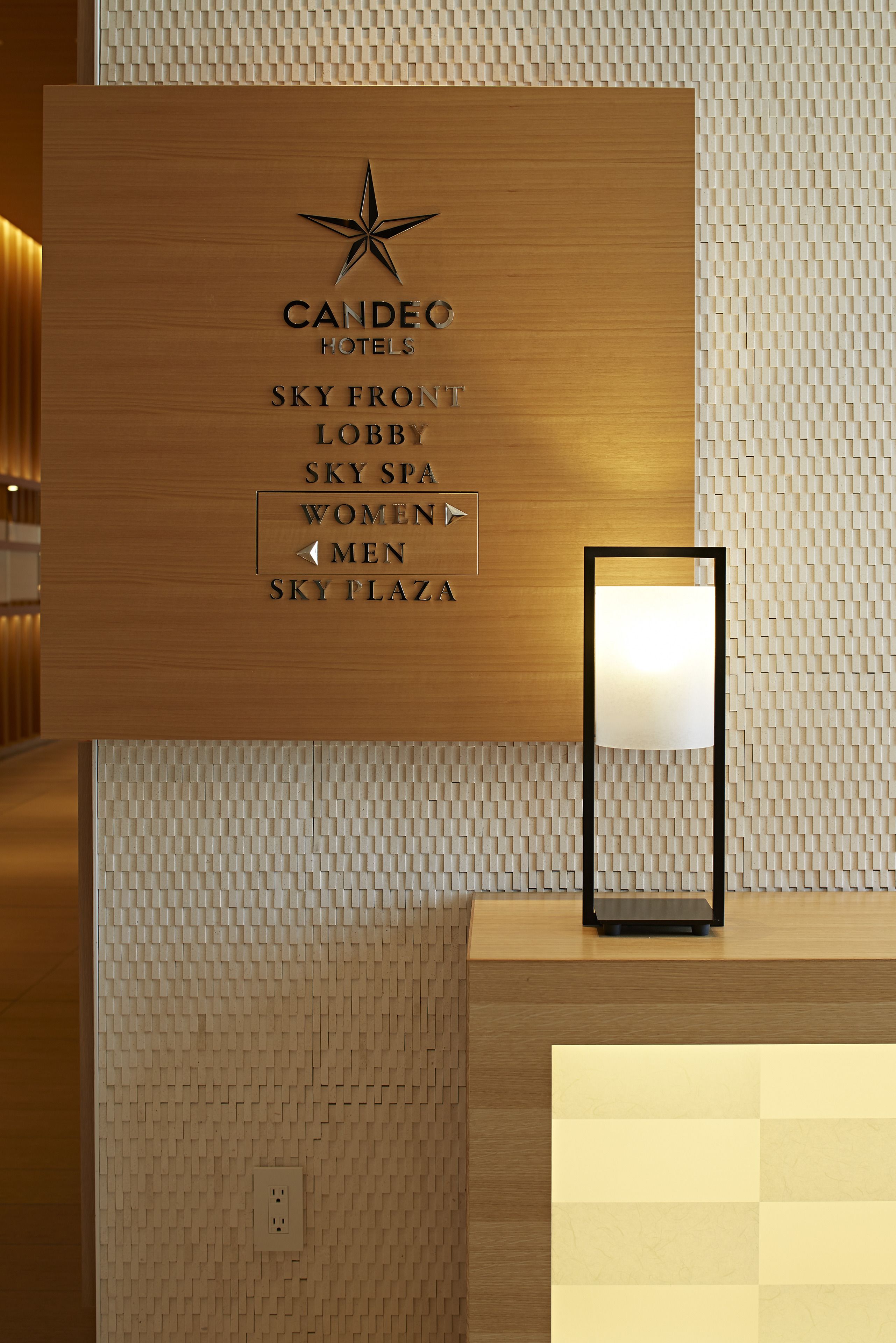 A reception desk with a wooden panel displaying the hotel name and directions to various amenities.