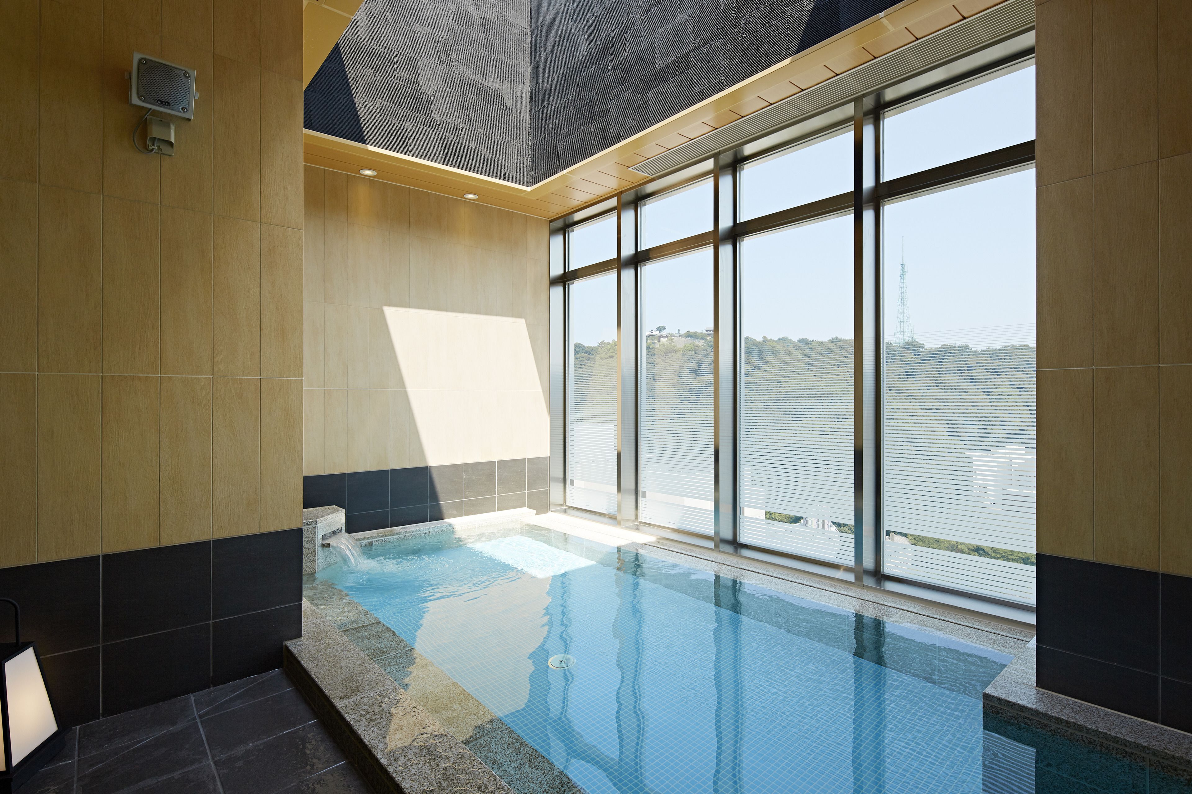 A modern indoor swimming pool with clear glass walls, a view of the cityscape, and a wooden interior design.