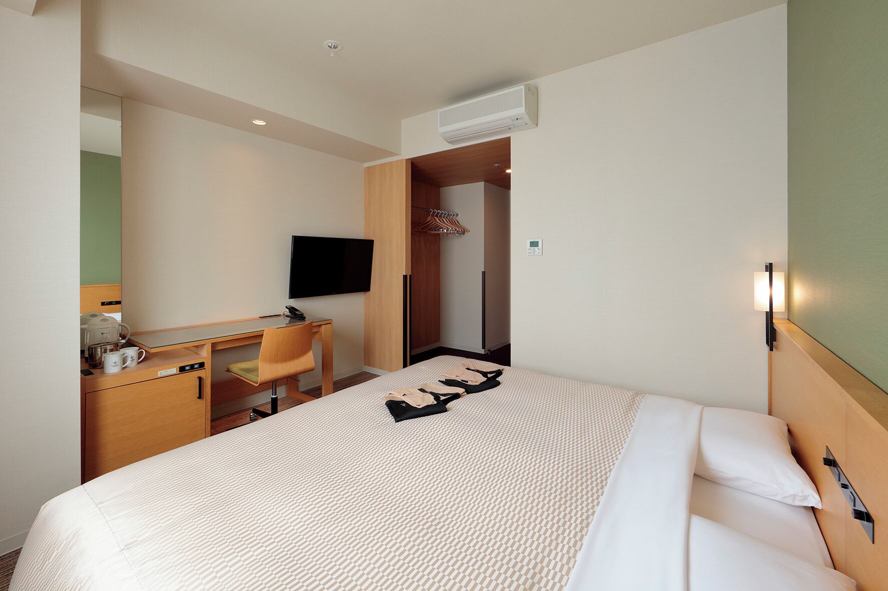 A hotel room with a bed, a desk, a chair, a television, and a wardrobe.