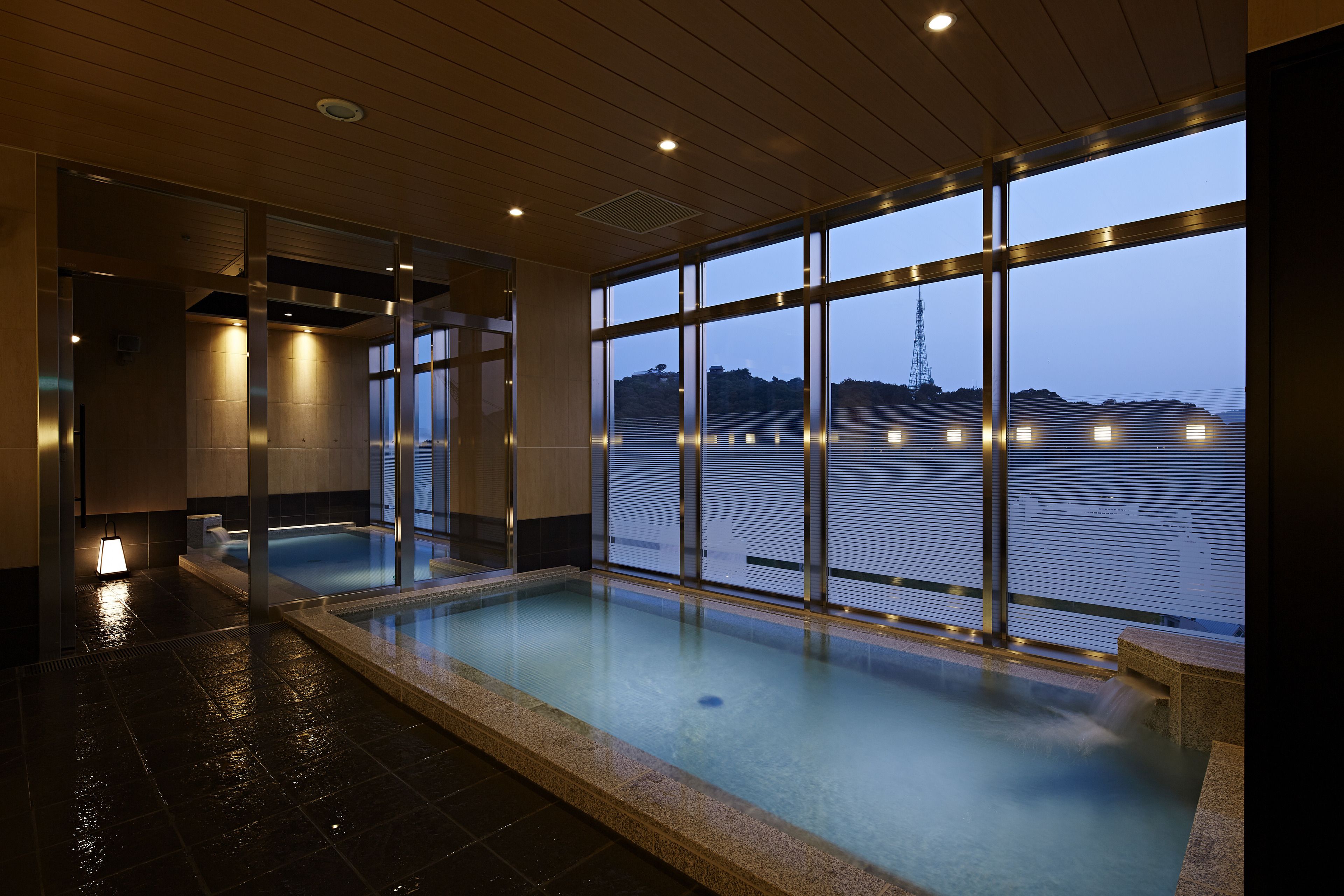 A modern indoor swimming pool with a view of a body of water and a tower in the distance.