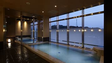 A modern indoor swimming pool with a view of a body of water and a tower in the distance.