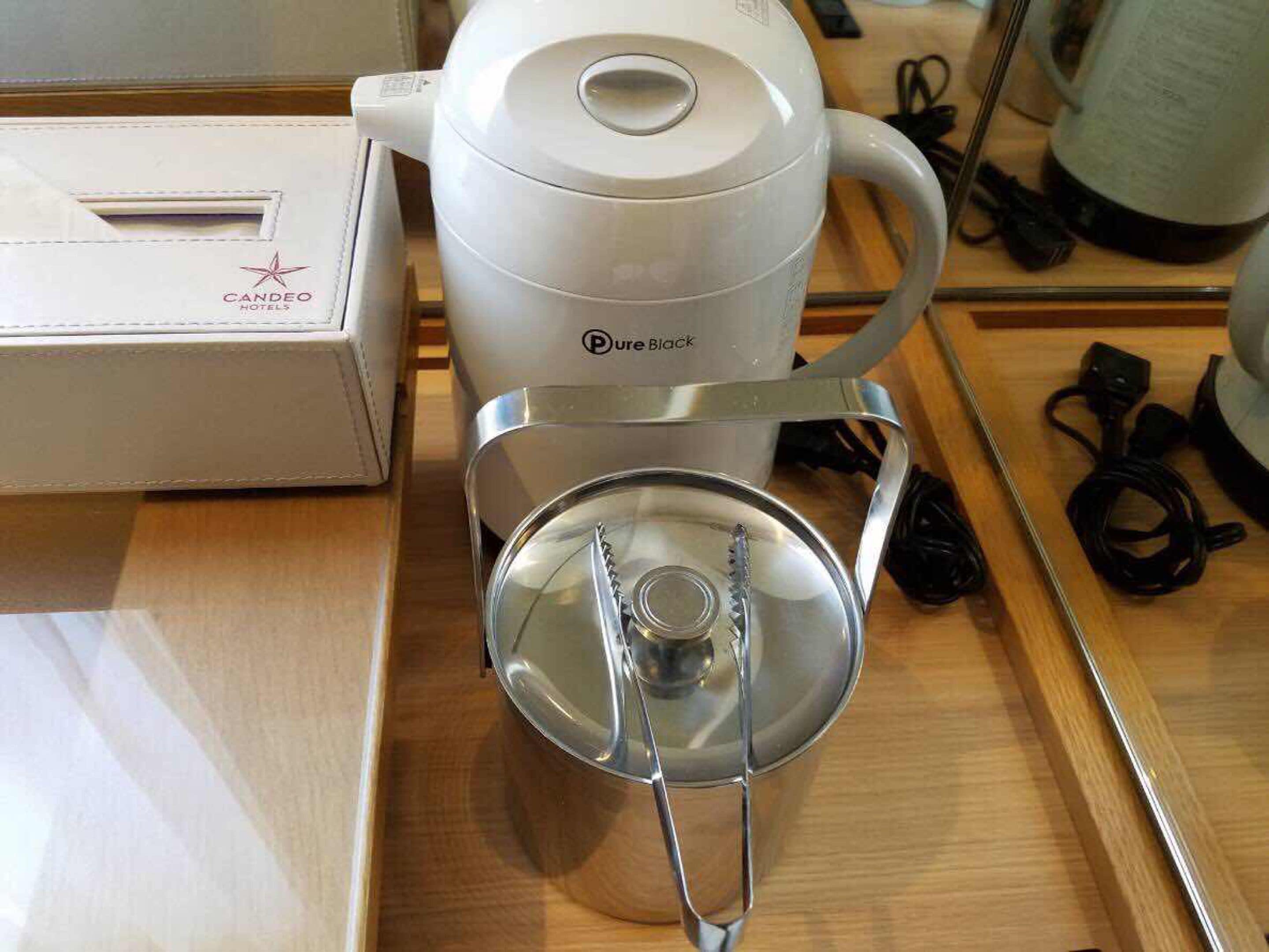 Een koffiezetapparaat met een transparante waterreservoir en een deksel, geplaatst op een houten tafel.