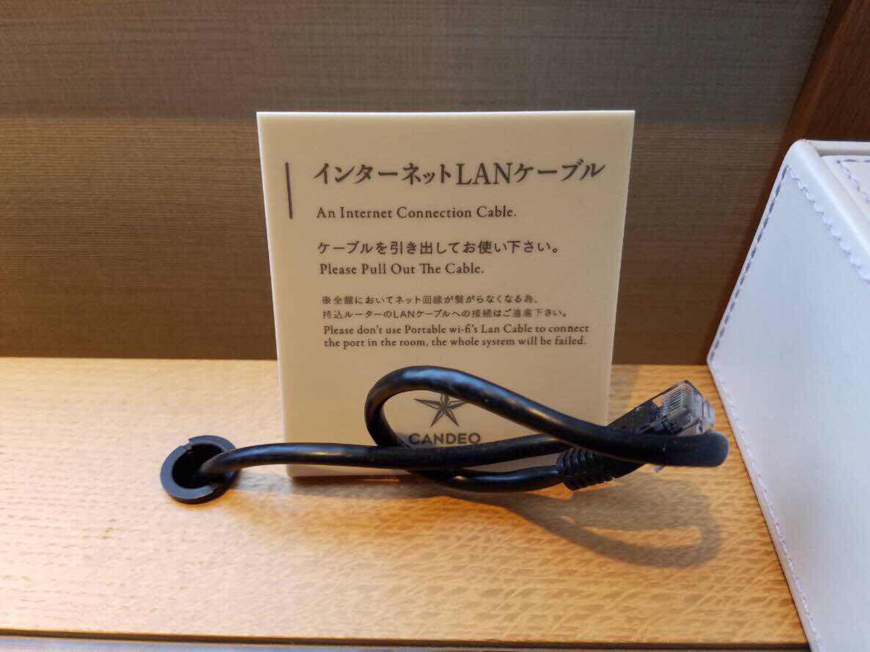 Cable LAN con una etiqueta en inglés y japonés, sobre una superficie de madera.