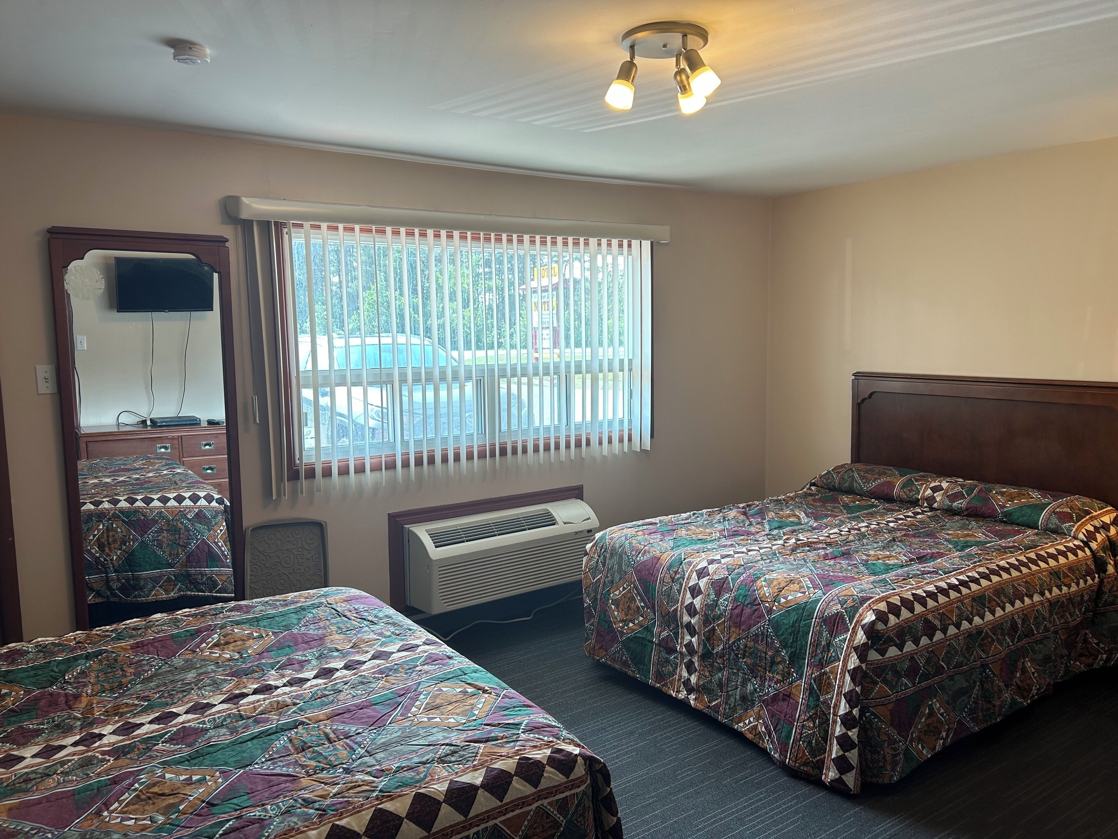 A hotel room with two beds, a large window with blinds, a ceiling fan, and a mounted television.