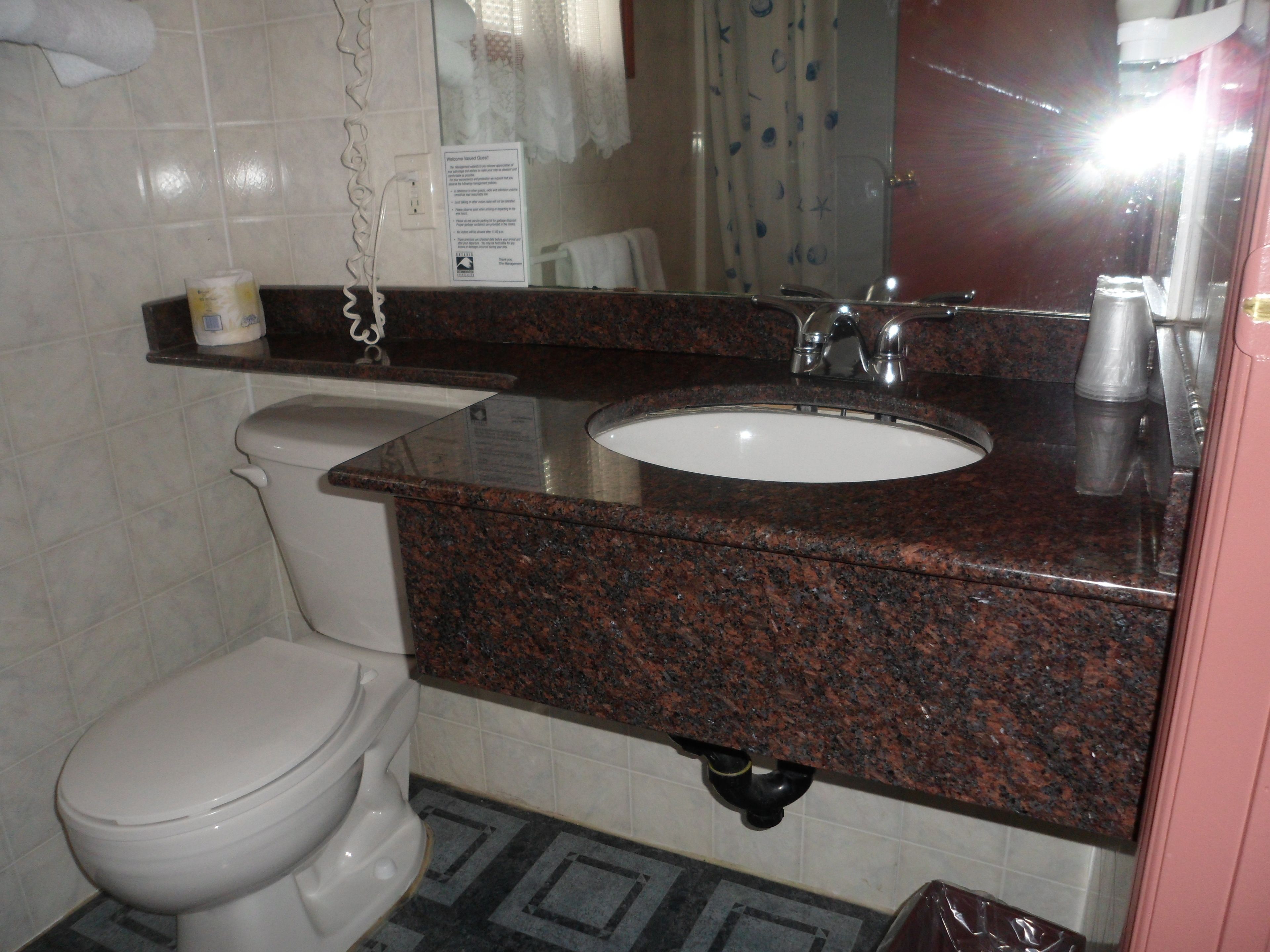 Un baño con un inodoro blanco, un lavabo con encimera de granito y un espejo encima.