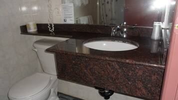 Un baño con un inodoro blanco, un lavabo con encimera de granito y un espejo encima.