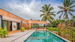 A modern house with a swimming pool, surrounded by tropical plants and palm trees. - Pacific Palms Luxury Villa (Rarotonga)