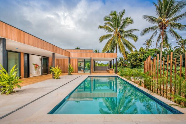A modern house with a swimming pool, surrounded by tropical plants and palm trees. - Pacific Palms Luxury Villa (Rarotonga)