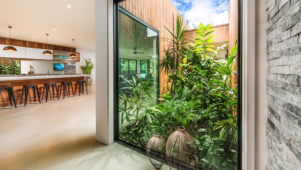 A modern kitchen with a glass door leading to a garden, wooden accents, and a bar area with stools. - Pacific Palms Luxury Villa (Rarotonga)