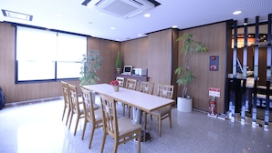 A conference room with a long table, chairs, a fire extinguisher, and a potted plant. - APA Hotel Nishimaizuru-Ekimae (Maizuru)