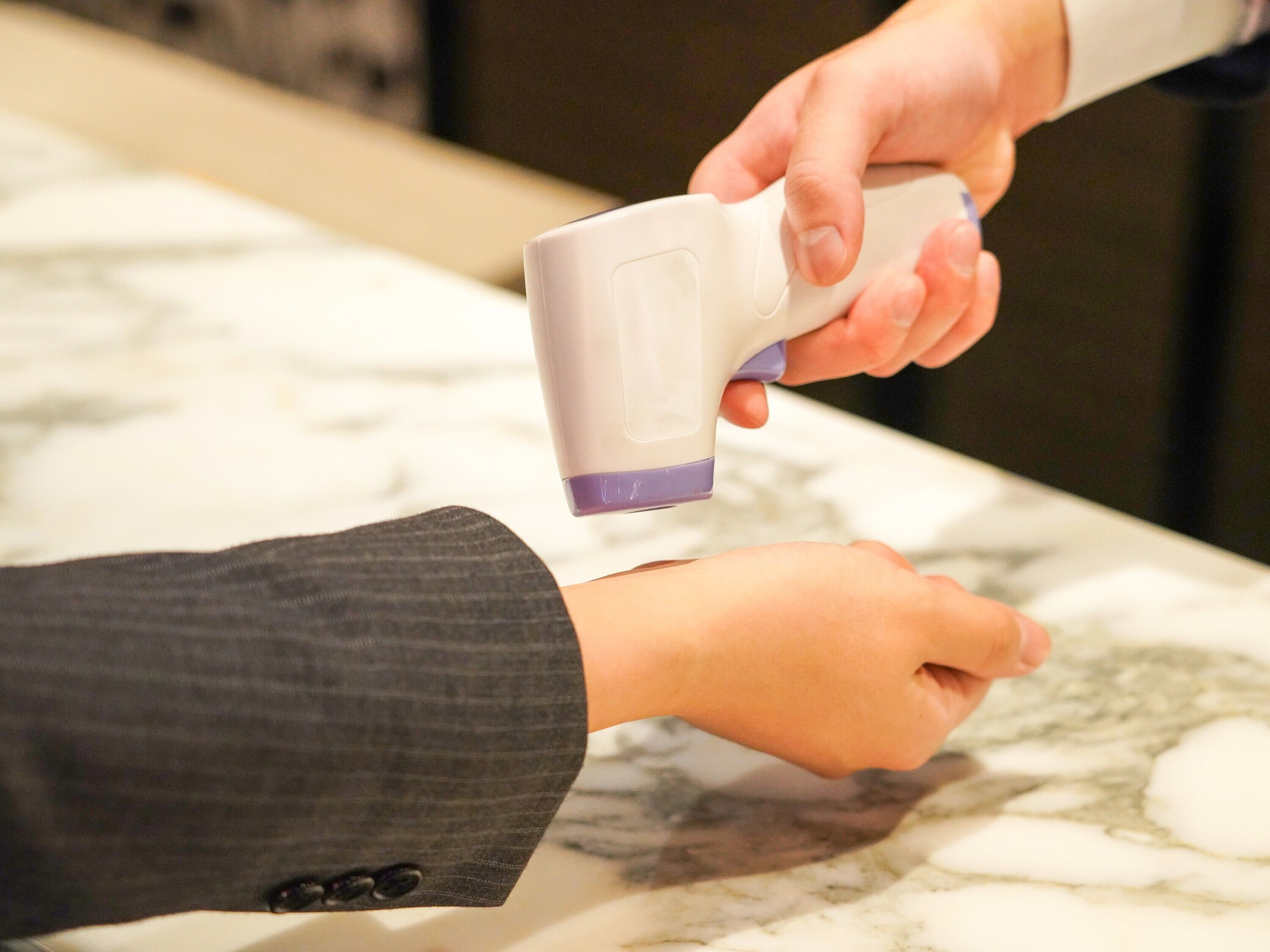 A person holding a white and purple object, possibly a device, over another person's hand.